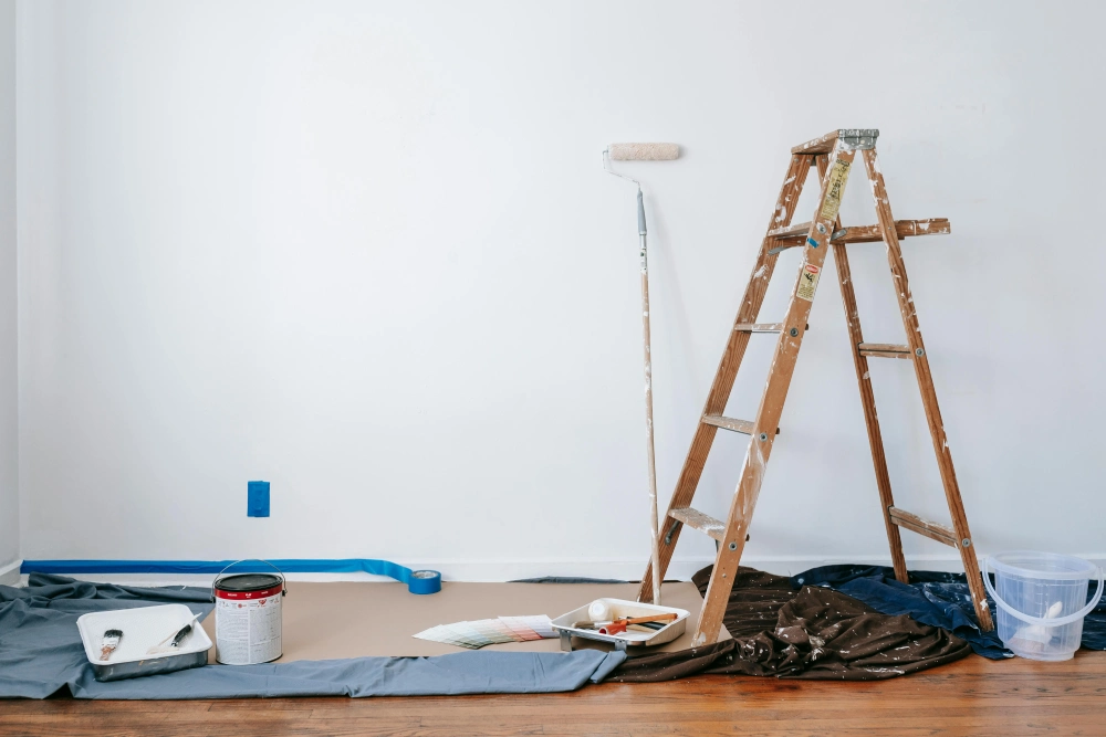 A ladder next to paint rollers and paint brushes