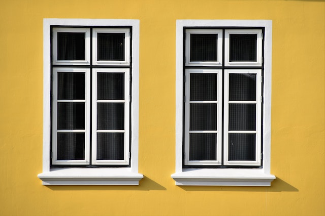 A yellow wall with two white windows