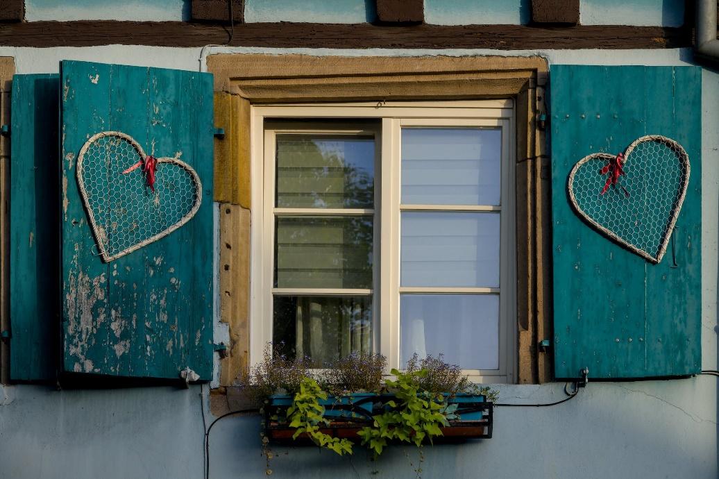 A window with blue shutters featuring white heart shapes.