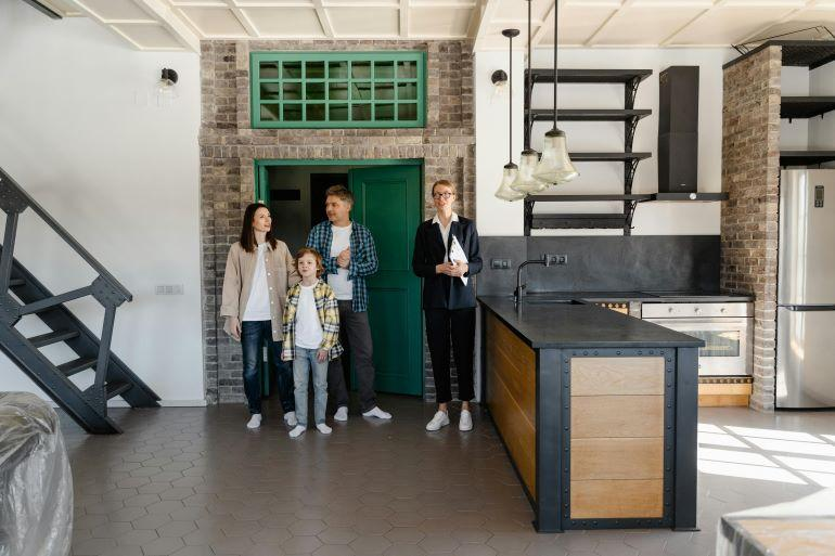 Family and designer standing in a renovated open kitchen with a modern island and industrial details during a home walkthrough.