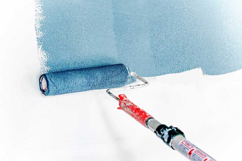 A paint roller applies blue paint to a white wall.