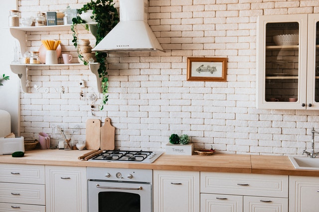 Kitchen with an exposed brick wall painted white, two cutting boards next to the stove, and white cabinets