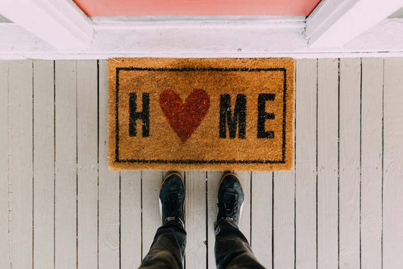 Man standing in front of a doormat with the word HOME