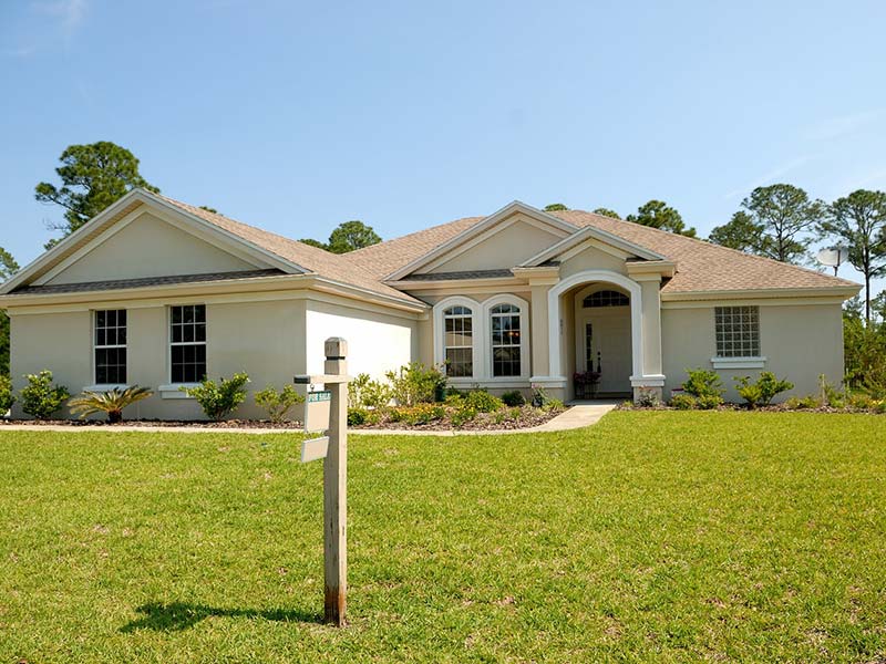 A contemporary house with a “for sale” sign in the front yard.