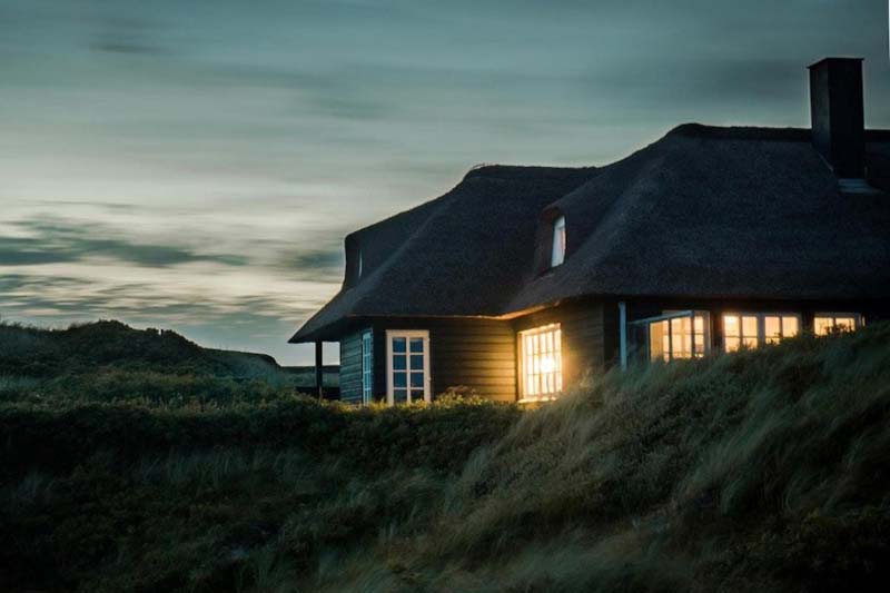 The house with fireplace surrounded by grass under the white and gray cloudy sky.