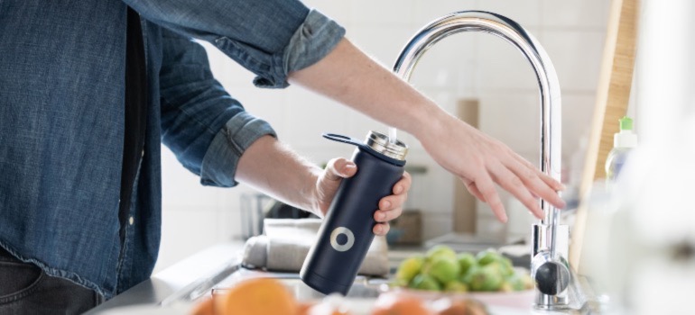 A person filling up a bottle with water from their faucet