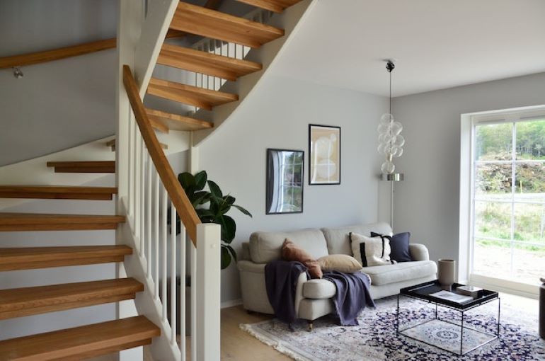 A white sofa next to a brown staircase leading up after you add a second story to your home