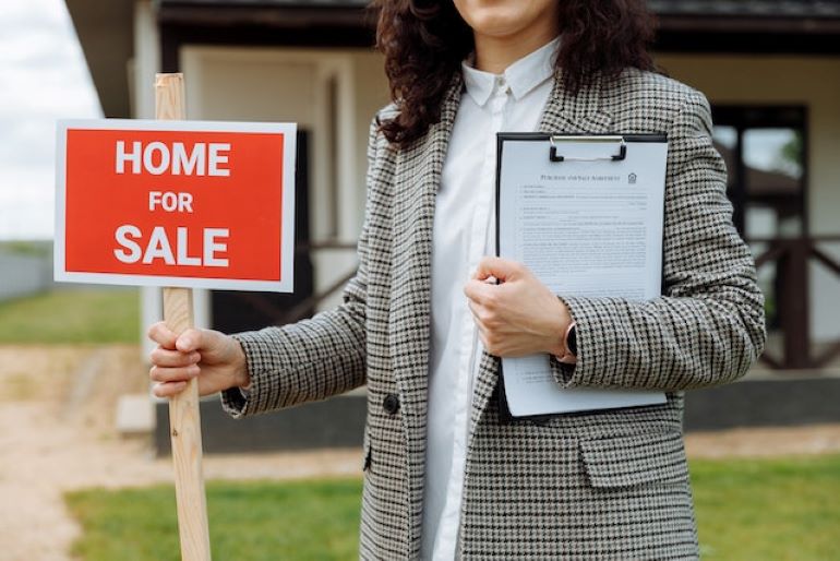A woman is holding a sign 'home for sale'