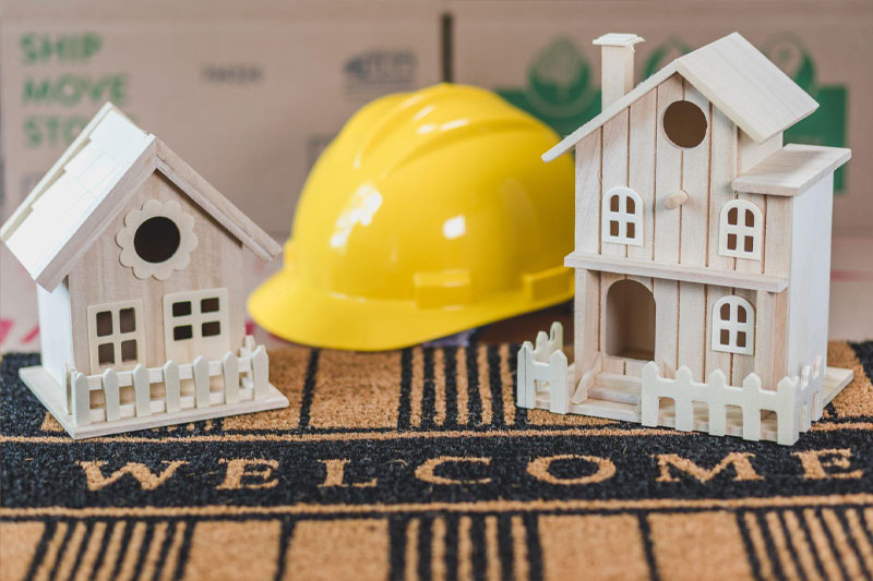 image of a construction hard hat and wood bird houses on a welcome carpet